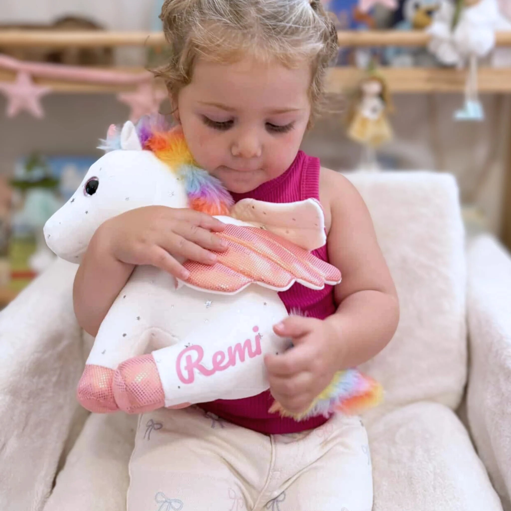 Girl hugging a personalized unicorn plush toy with pink mane and name Remi on the belly.